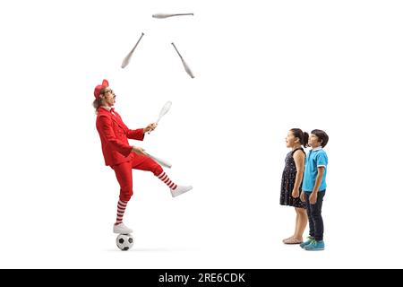 Kinder beobachten einen Mann in einem roten Anzug, der auf einem Fußball steht und isoliert auf weißem Hintergrund jongliert Stockfoto