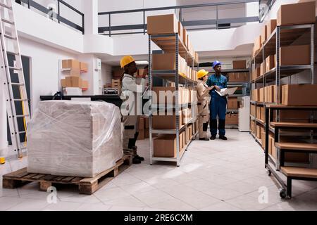 afroamerikanische und kaukasische Lagerarbeiter scannen Barcodes von Paketen und erstellen Inventar. Verschiedene Lagermitarbeiter tragen Uniform, die im Lager arbeiten Stockfoto