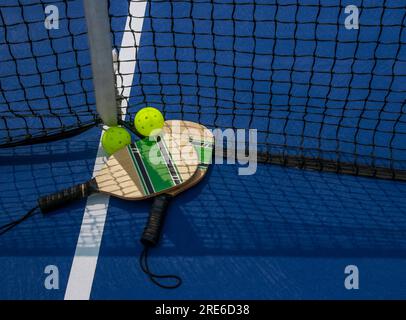 Zwei Pickleball-Paddel und zwei Yello-Pfiffle-Bälle auf einem Platz in der Nähe des Netzes Stockfoto