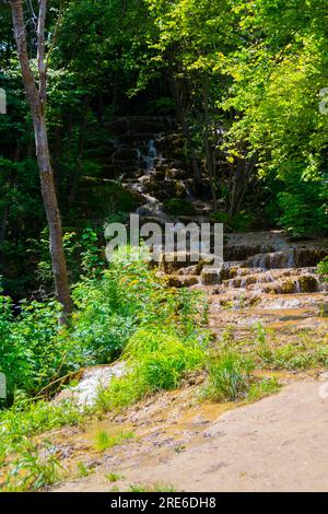 Wagen Sie sich in eine magische Welt der Waldwasserfälle, wo die Kunst der Natur atemberaubende türkisfarbene Seen enthüllt. Tauchen Sie ein in das ruhige B Stockfoto