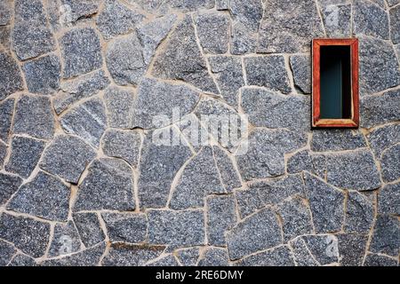 Ein kleiner eleganter lackierter Holzfensterrahmen in einer handgefertigten Steinwand, ein Beispiel für einfache und minimalistische moderne Architektur, Details. Stockfoto