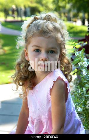 Das kleine Engelchen sieht in die Kamera. Sie denkt und schaut in die Ferne. Sie hat blonde Haare und Korkenzieher. Stockfoto