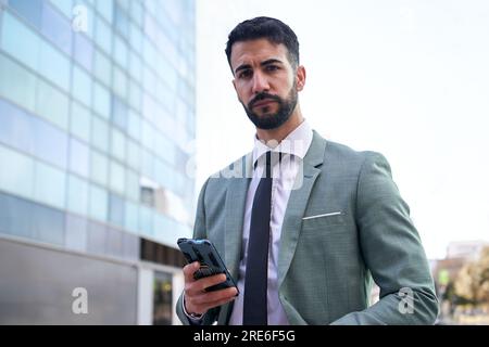 Porträt eines jungen, gutaussehenden, selbstbewussten Geschäftsmannes, der während einer Pause im Freien mit dem Handy telefoniert. Stockfoto
