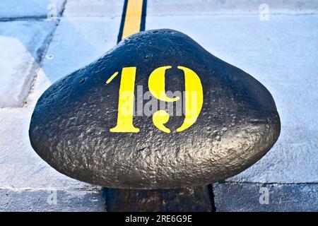 Nummer 19, neunzehn, Schablonen-gelbe Ziffer, gemalt auf einem großen gewerblichen Hafenpfosten. Stockfoto