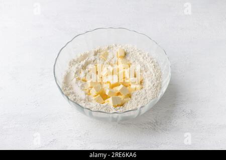 Glasschüssel mit Mehl und Butterwürfeln auf hellgrauem Hintergrund. Köstliche hausgemachte Kuchen werden Schritt für Schritt zubereitet. Stockfoto