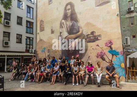 PLOWDIW, BULGARIEN - 29. JULI 2019: Menschen sitzen unter einem Graffiti an einer Wand im kreativen Viertel Kapana in Plowdiw, Bulgarien Stockfoto