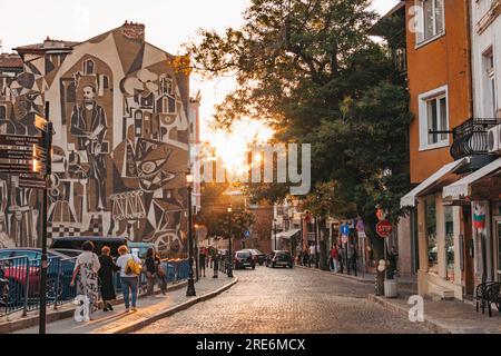 Die Sonne geht in einer alten Stadtstraße in Plowdiw, Bulgarien, unter. Mit einem großen Wandgemälde an der Seite eines Apartments Stockfoto