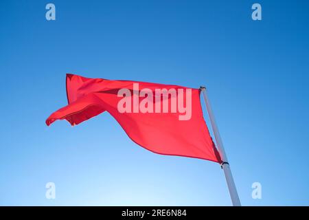 Eine rote Flagge im Wind, isoliert auf hellblauem Himmelshintergrund. Stockfoto