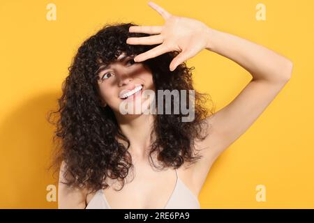 Wunderschöne junge Frau, die sich mit der Hand von Sonnenlicht vor orangefarbenem Hintergrund schattiert Stockfoto