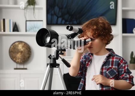 Süßer kleiner Junge, der Sterne durch ein Teleskop im Zimmer sieht Stockfoto