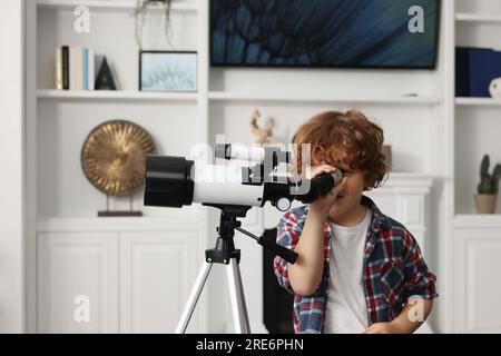 Süßer kleiner Junge, der Sterne durch ein Teleskop im Zimmer sieht Stockfoto