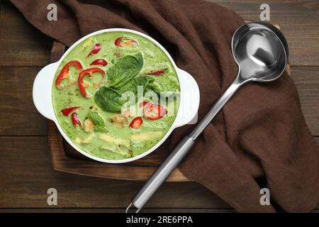 Kochtopf mit leckerer grüner Curry-Hühnersuppe und Kelle auf einem Holztisch, flach liegend Stockfoto