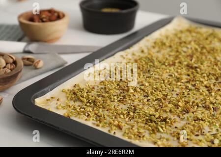 Ich mache köstliche Baklava. Backform mit Teig und gehackter Nussmischung auf weißem Tisch, Nahaufnahme Stockfoto