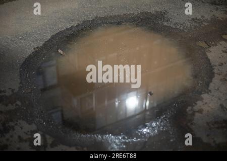 Pfütze in der Sonne. Schmutziges Wasser. Pfütze auf der Straße. Schmutz auf Asphalt. Stockfoto