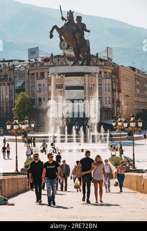 Menschen, die auf dem Hauptplatz von Skopje, Nordmazedonien, spazieren gehen. Eine Skulptur von Alexander dem Großen ist dahinter zu sehen. Stockfoto