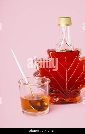 Flasche und Löffel in einem Glas leckeren Ahornsirups auf rosa Hintergrund Stockfoto