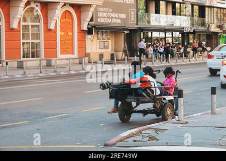 Obdachlose Kinder sitzen auf einem motorisierten Dreirad auf einer Straße in Skopje, Nordmazedonien Stockfoto