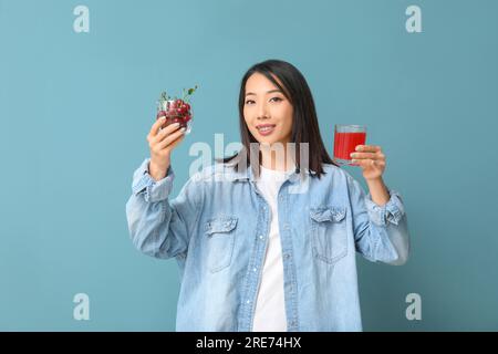 Wunderschöne asiatische Frau mit Kirschen und einem Glas Saft auf blauem Hintergrund Stockfoto