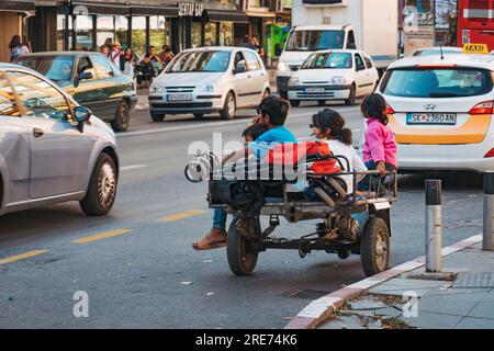 Obdachlose Kinder sitzen auf einem motorisierten Dreirad auf einer Straße in Skopje, Nordmazedonien Stockfoto