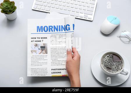 Frau, die am Arbeitsplatz Zeitung liest, mit einer Tasse Kaffee auf grauem Hintergrund Stockfoto