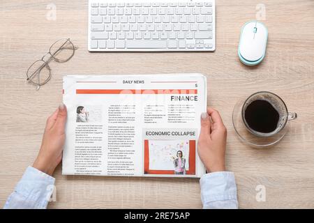 Frau, die am Arbeitsplatz Zeitung liest, mit einer Tasse Kaffee auf Holzhintergrund Stockfoto