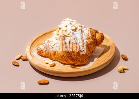 Holzteller mit süßem Croissant mit Puderzucker und verschiedenen Nüssen auf rosa Hintergrund Stockfoto