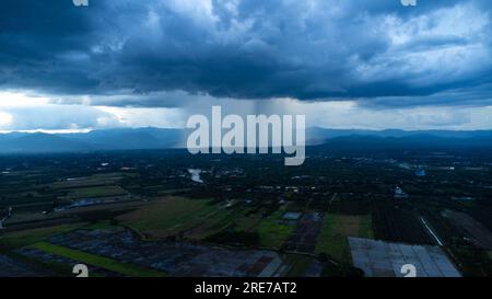 Panoramablick aus der Vogelperspektive auf Gemeinde und Ackerland mit riesigen Sturmwolken im Hintergrund. Luftaufnahme des Regens über einer ländlichen Gemeinde. Regenwolken Stockfoto