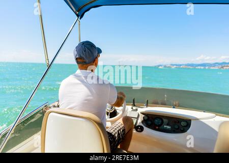 Bach-Blick auf einen Mann mittleren Alters, der eine Luxusmotoryacht fährt. Kapitän am Steuer des Motorboots. Bild mit selektivem Fokus Stockfoto