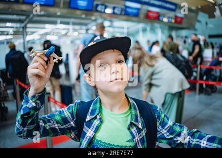 Lächelnder, glücklicher, weißer Junge vor der Reise mit einem Flugzeug, das Spielzeugflugzeug in der Flughafenhalle vor dem Abflug hält. Bild mit selektivem Fokus Stockfoto