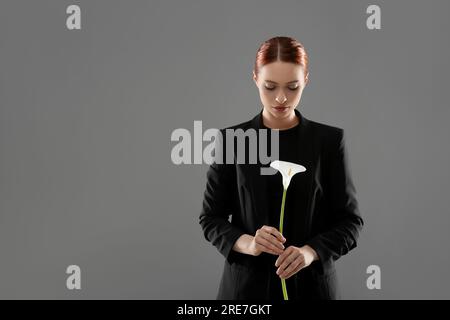 Traurige Frau mit Calla-Lilienblume auf grauem Hintergrund, Platz für Text. Beerdigungszeremonie Stockfoto