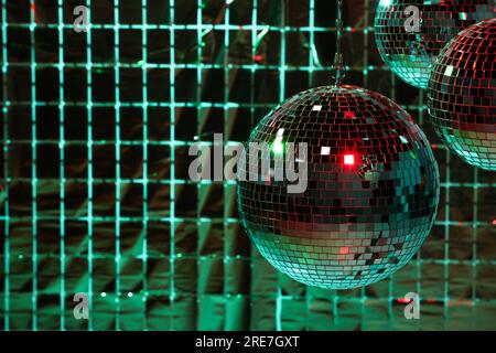 Glänzende Disco-Bälle an einem Partyvorhang unter farbigen Lichtern, Platz für Text Stockfoto