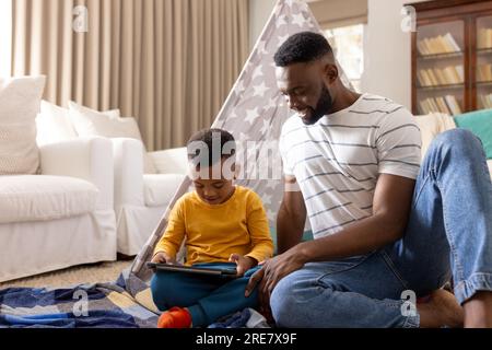 Glücklicher afroamerikanischer Vater und Sohn, der zu Hause ein Tablet benutzt Stockfoto