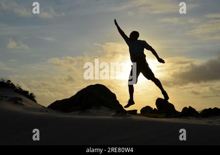 Ein gesprungener Mann, der bei Sonnenaufgang nach den Sternen greift. Stockfoto