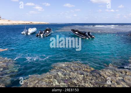 Drei aufblasbare Boote stehen leer vor Anker an einem Korallenriff mit kristallklarem Wasser. Stockfoto