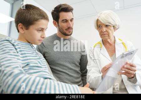 Eine Ärztin mit Klemmbrett spricht über Vater und kleinen Jungen Stockfoto