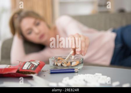 eine frau auf dem Sofa, die im Aschenbecher nach einer Zigarette greift Stockfoto