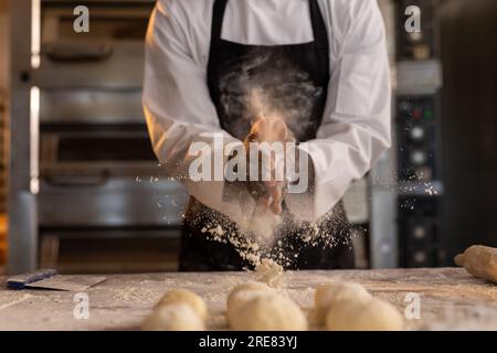 afroamerikanischer Bäcker in Bäckereiküche klatscht Hände mit Mehl Stockfoto