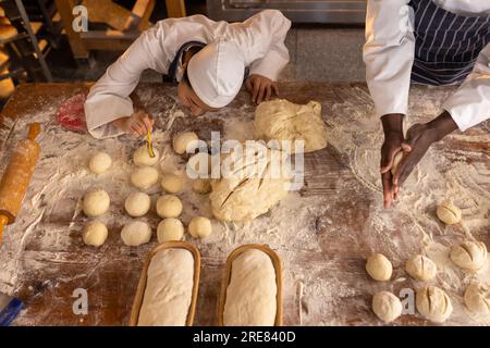 Glückliche, vielfältige Bäcker, die Schürzen in der Bäckerei tragen und Teigrollen machen Stockfoto