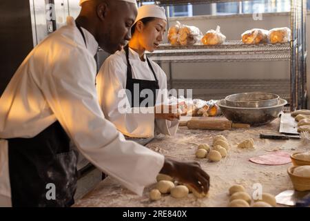 Glückliche, vielfältige Bäcker, die Schürzen in der Bäckerei tragen und Teigrollen machen Stockfoto