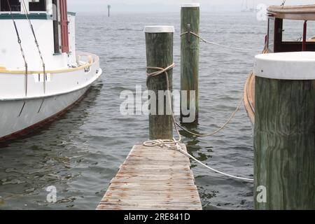 Ein Foto eines kleinen schmalen Holzdecks, das zum Meer mit Booten auf beiden Seiten führt. Stockfoto