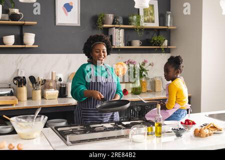 Glückliche afroamerikanische Mutter und Tochter backen Pfannkuchen in der Küche zu Hause Stockfoto