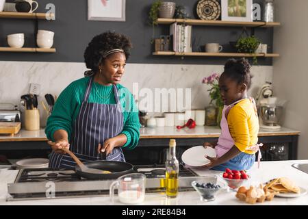 Glückliche afroamerikanische Mutter und Tochter backen Pfannkuchen in der Küche zu Hause Stockfoto