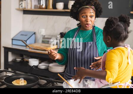 Glückliche afroamerikanische Mutter und Tochter backen Pfannkuchen in der Küche zu Hause Stockfoto