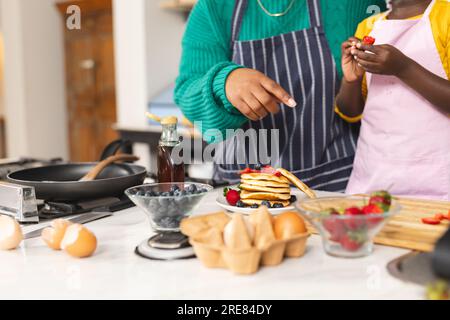 Mittelteil afroamerikanischer Mutter und Tochter, die Pfannkuchen in der Küche zu Hause backen Stockfoto