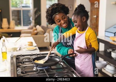 Glückliche afroamerikanische Mutter und Tochter backen Pfannkuchen in der Küche zu Hause Stockfoto