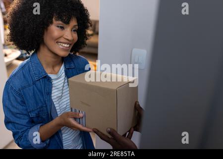 Glückliche, birassische Frau, die zu Hause ein Paket erhält Stockfoto