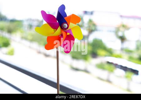 Bunte Windrad dreht sich im Wind auf einem Balkon mit einem verschwommenen hellen Hintergrund im Freien. Perfektes Spielzeug für die Gartendekoration für Kinder. Stockfoto