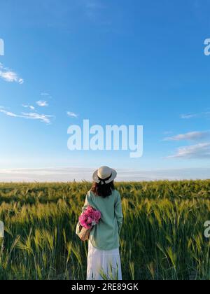 Rückansicht einer stilvollen Frau mit Korb und Pfingstrosen auf einem Feld in Weißrussland Stockfoto