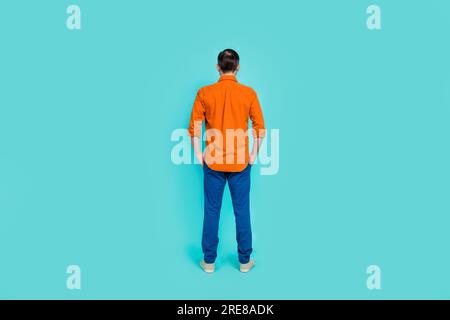 Foto in Gesamtgröße eines Geschäftsmanns mit formeller Kleidung, orangefarbenes Hemd mit blauer Denimjeans, isolierte Handtaschen auf cyanfarbenem Hintergrund Stockfoto