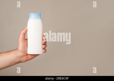 Ein Mann, der eine weiße Flasche Lotion oder Shampoo in der Hand hält, grauer Hintergrund mit Kopierbereich Stockfoto